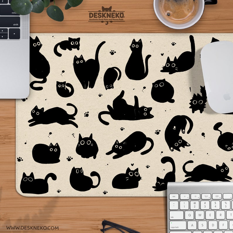 Puede incluir: Alfombrilla de rat&oacute;n beige con un patr&oacute;n de siluetas de gatos negros en varias poses. La alfombrilla tiene un logotipo en la parte superior y una direcci&oacute;n web en la parte inferior. Tambi&eacute;n se ven un rat&oacute;n y un teclado blancos.