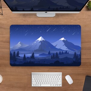 May include: A rectangular mouse pad featuring a mountain landscape design under a starry night sky. The design includes snow-capped mountains, trees, and a lake, all in shades of blue and white. A computer keyboard, mouse, and monitor are visible.