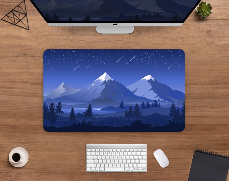 May include: A rectangular mouse pad featuring a mountain landscape design under a starry night sky. The design includes snow-capped mountains, trees, and a lake, all in shades of blue and white. A computer keyboard, mouse, and monitor are visible.