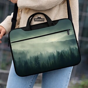 May include: Black laptop bag with a forest scene design. The bag has a black handle and a shoulder strap. The image on the bag depicts a misty forest with tall trees. The bag has the text "DESKNEKO" and "WWW.DESKNEKO.COM".