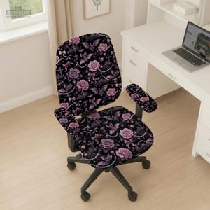 May include: An office chair with a black base and a patterned seat and back. The pattern features pink and purple roses, bats, and pearls on a black background. The chair has armrests with the same pattern.