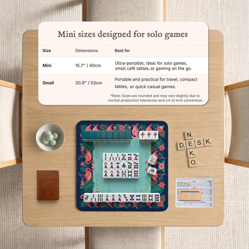 May include: A tabletop display featuring a mini Mahjong set with a teal playing surface and flamingo and floral design. The set includes tiles, dice, and a small brown notebook. The text on the display reads "Mini sizes designed for solo games."