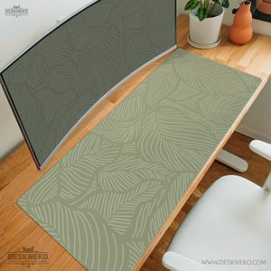 Pode incluir: Tapete de mesa retangular com fundo verde claro e um padrão repetido de desenhos brancos semelhantes a folhas. O tapete está colocado numa secretária de madeira, com um monitor de computador curvo e uma cadeira branca.
