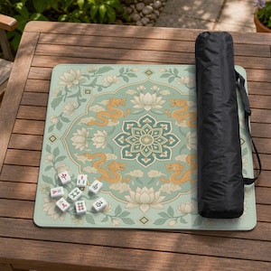 May include: A square mahjong mat featuring a light green background with a central mandala, four golden dragons, and white lotus flowers. Seven white mahjong tiles with red and green characters are placed on the mat, alongside a black carrying bag.