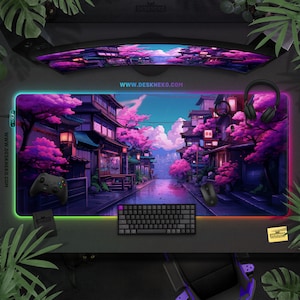 May include: A large rectangular gaming mouse mat featuring a colourful illustration of a Japanese street scene with cherry blossom trees. The mat has an LED border, a black keyboard, a mouse, and a game controller. The website address www.deskneko.com is visible.