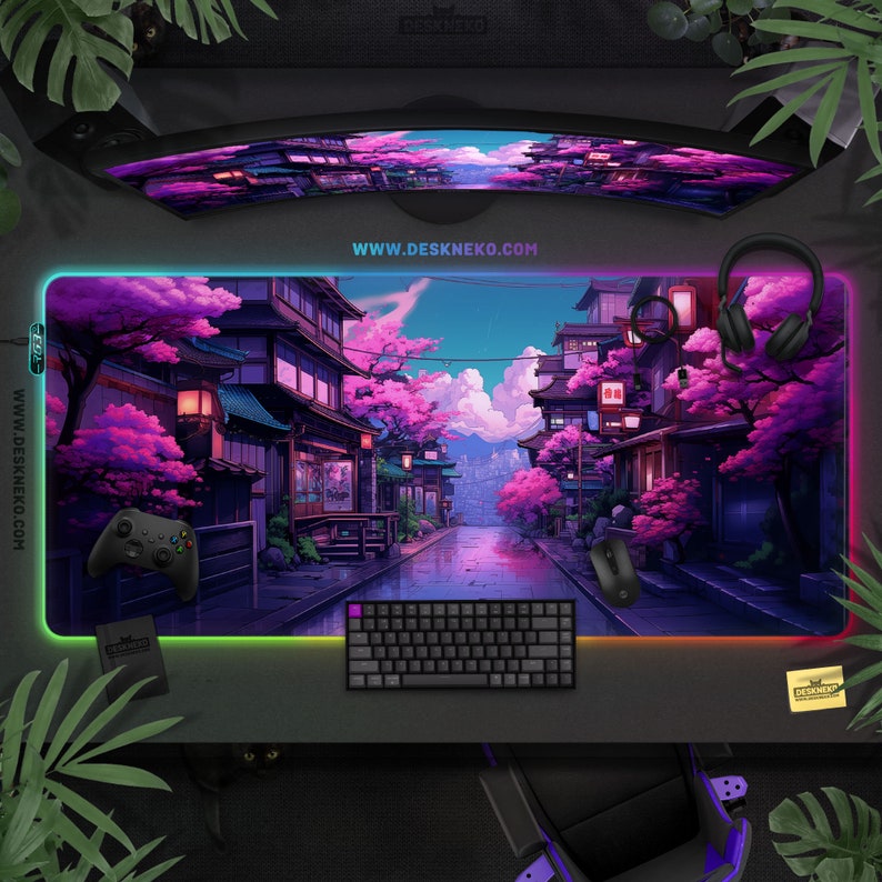 May include: A large rectangular gaming mouse mat featuring a colourful illustration of a Japanese street scene with cherry blossom trees. The mat has an LED border, a black keyboard, a mouse, and a game controller. The website address www.deskneko.com is visible.