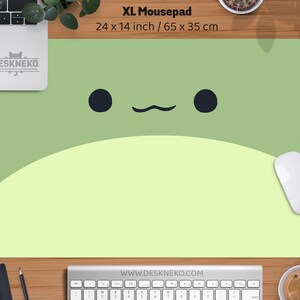 May include: XL mousepad, 24 x 14 inches, featuring a cute cartoon frog face design. The mousepad has a light green and yellow color scheme with black eyes and a curved mouth. The brand name "DESKNEKO" is visible.