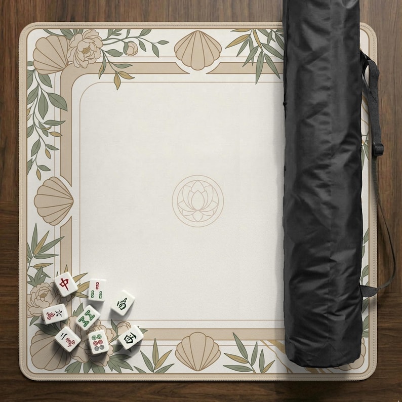 May include: A beige Mahjong game mat with a floral and seashell border design. The mat has a central lotus flower emblem and includes a black carrying case. Several Mahjong tiles are scattered on the mat.