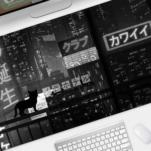 Op de afbeelding: Zwart-witte bureaumat met een nachtelijk stadsgezicht, Japanse tekst en neonreclame. Een zwart katten silhouet staat op een balkon. Het woord "KAWAII" staat in een neonreclame. Een toetsenbord en muis staan op de voorgrond.