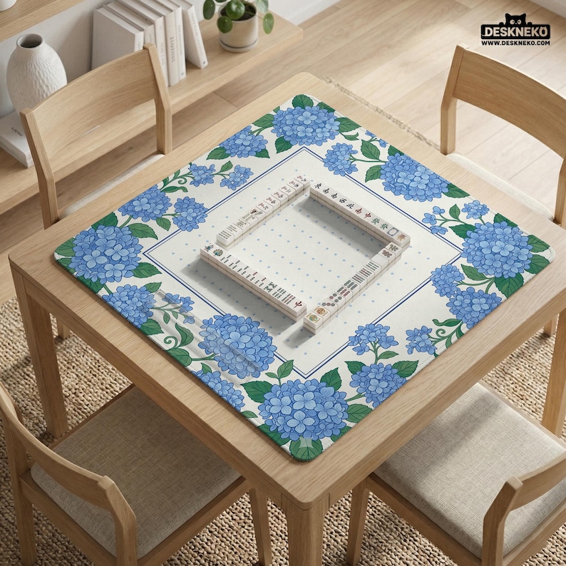 May include: A square mahjong table mat with a floral hydrangea design in blue and green. The mat is on a wooden table with a set of mahjong tiles arranged on top. The text "DESKNEKO" is visible in the top right corner.