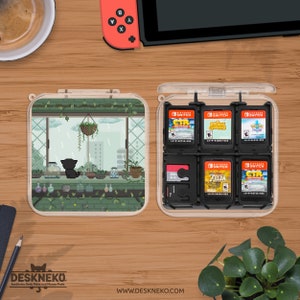 May include: Clear plastic Nintendo Switch game cartridge case with a pixelated cat scene. The case is open, showing game cartridges and a memory card. The case is on a wooden surface with a coffee cup and a Switch controller.