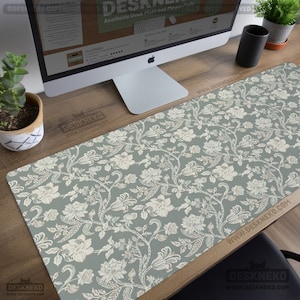 May include: Aesthetic desk mat with a floral pattern. The mat features a light green background with a repeating design of white flowers and vines. The brand name "DeskNeko" is visible on the mat and the website address is also visible.
