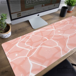 Puede incluir: Alfombrilla de escritorio estética con un diseño rosa similar al agua y contornos blancos. La alfombrilla rectangular está colocada sobre un escritorio de madera. El texto "DeskNeko" y "Aesthetic Desk Mats and Mouse Pads" es visible.