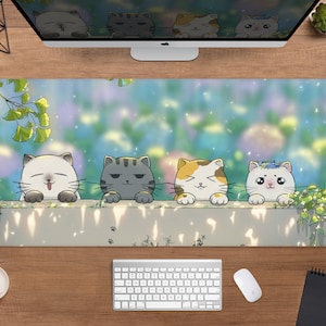 May include: A long rectangular desk mat featuring an illustrated design of four cartoon cats peering over a wall. The cats have different expressions and colors, set against a blurred background of foliage and a light blue sky. The mat is on a wooden desk.