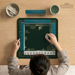 Pode incluir: Uma pessoa jogando Mahjong em um tapete verde com pe&ccedil;as turquesa. O conjunto do jogo inclui uma tigela com dados e palitos e uma x&iacute;cara pequena. O tapete tem detalhes dourados e caracteres chineses.