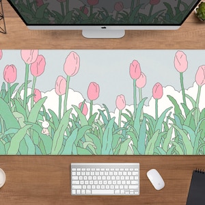 Puede incluir: Alfombrilla de ratón rectangular con una ilustración caprichosa de tulipanes rosas en un campo con un pequeño conejo blanco. El fondo es un cielo azul claro con nubes blancas, y las hojas son verdes. Se ven un teclado, un ratón y una taza de café.