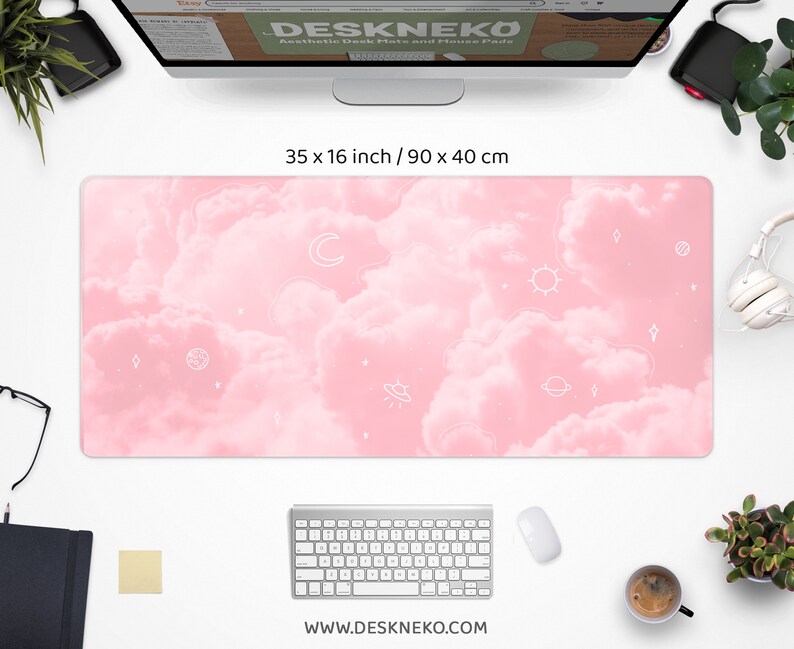 May include: Aesthetic desk mat with a pink cloud design and white celestial illustrations. The mat measures 35 x 16 inches. The website address www.deskneko.com is printed at the bottom. A keyboard, mouse, and other office supplies surround the mat.