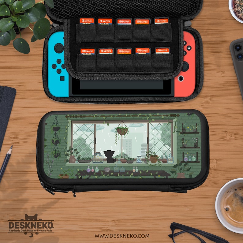 May include: Black Nintendo Switch carry case with a whimsical design of a cat looking out a window. The case is open, showing a Switch console and game cartridge storage. The top case is black with a zipper.