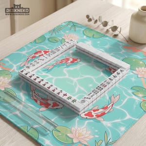 May include: A rectangular desk mat featuring a light blue water surface pattern with koi fish, lotus flowers, and lily pads. A square arrangement of white mahjong tiles with black and red characters and symbols is placed on the mat surface.