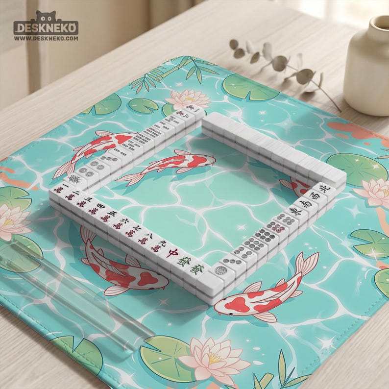 May include: A rectangular desk mat featuring a light blue water surface pattern with koi fish, lotus flowers, and lily pads. A square arrangement of white mahjong tiles with black and red characters and symbols is placed on the mat surface.