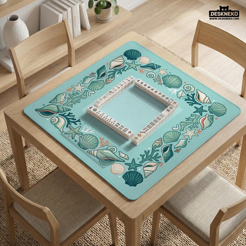 May include: A square, pale blue game mat featuring a border of seashells, starfish, and coral. A wooden frame with game pieces is in the centre. The mat is on a wooden table with chairs. The text "DESKNEKO" is in the upper right corner.