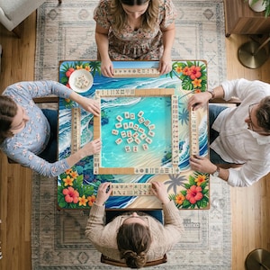 May include: A top-down view of a Mahjong game in progress. The game board features a tropical beach scene with palm trees and hibiscus flowers. Four people are seated around the table, each with a hand of tiles.