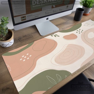 Puede incluir: Alfombrilla de escritorio est&eacute;tica con fondo crema y formas abstractas en tonos melocot&oacute;n y verde oliva. La alfombrilla presenta el texto "Aesthetic Desk Mats and Mouse Pads" y el logotipo de DeskNeko. La alfombrilla est&aacute; sobre un escritorio de madera.
