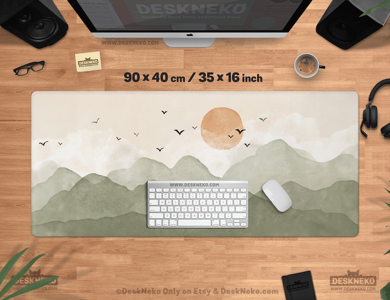 May include: A rectangular desk mat with a landscape design featuring mountains, a sun, and birds. The mat is 35 x 16 inches and has the text "DESKNEKO" and "WWW.DESKNEKO.COM". The color palette includes beige, green, and brown.