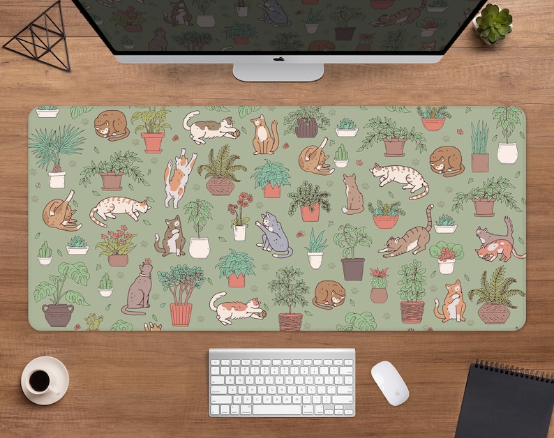 Puede incluir: Alfombrilla de rat&oacute;n rectangular con un fondo verde claro con un patr&oacute;n de gatos de dibujos animados y plantas en macetas. Los gatos est&aacute;n en varias poses, y las plantas est&aacute;n en macetas marrones. Se ven un teclado, un rat&oacute;n y una taza de caf&eacute;.