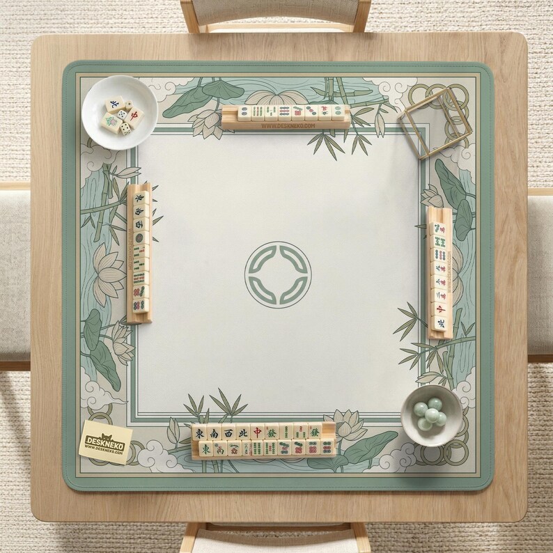 May include: A square wooden Mahjong table with a green and white floral design mat. The mat features lotus flowers, bamboo, and a central circular emblem. The table is set with tiles, dice, and small bowls.