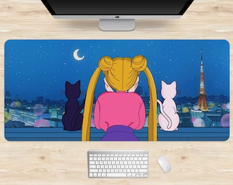 May include: A rectangular desk mat featuring an anime-style illustration. The design shows a character with blonde pigtails, a pink top, and a purple skirt, gazing at a cityscape with two cats. The background is a night sky with a crescent moon and stars.