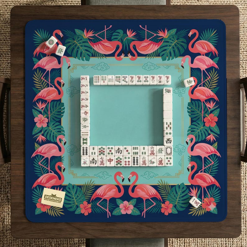 May include: A blue Mahjong game mat with a flamingo and tropical leaf design. The mat has a turquoise center and is surrounded by pink flamingos, flowers, and green leaves. The mat has a rectangular shape and is surrounded by a wooden frame.