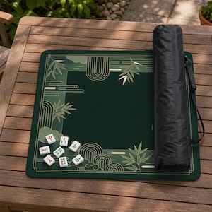 May include: A green Mahjong mat with a decorative gold bamboo and cloud design. The mat is rectangular and has a black carrying case. Several Mahjong tiles are scattered on the mat.
