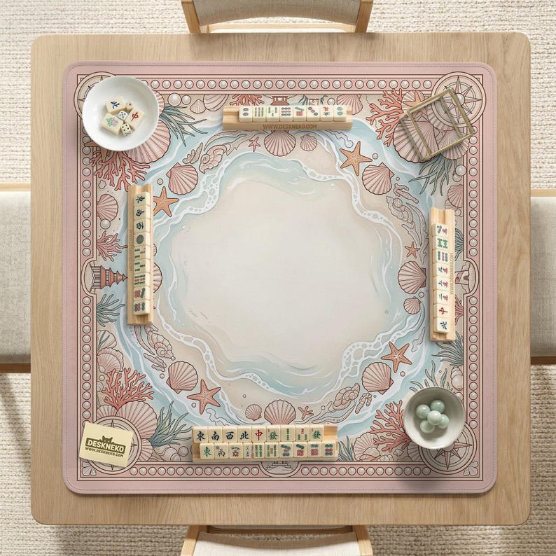 May include: A square mahjong game mat with a beach-themed design. The mat features a light pink border with a repeating circle pattern. The center has a beach scene with seashells, starfish, and coral. Mahjong tiles and bowls are placed around the mat.