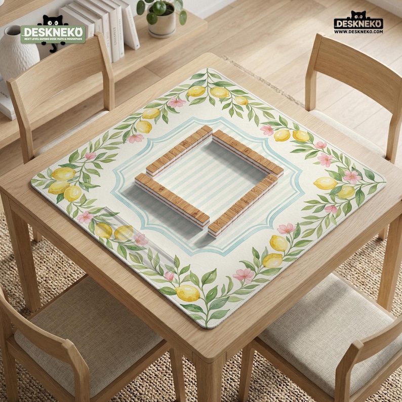 May include: A square table mat with a lemon and floral design. The mat features a light blue and white striped center, surrounded by a border of lemons, pink flowers, and green leaves. The mat has a wooden frame in the center.