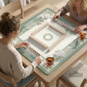 May include: A wooden mahjong table with a green and white floral design. Two people are playing mahjong, with tiles arranged on the table. The table has a light wood finish and is surrounded by chairs.