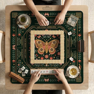 May include: A dark green mahjong mat featuring a central butterfly illustration, floral patterns, and game instructions. The mat includes a square tile wall, a tile rack with Chinese characters, two tea cups, and a small wooden case on a table.