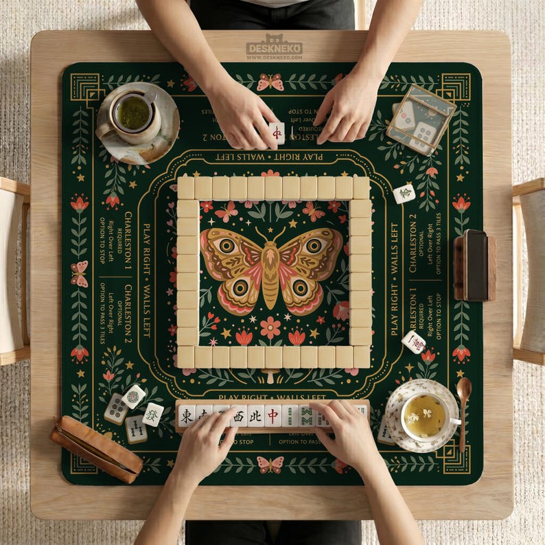 May include: A dark green mahjong mat featuring a central butterfly illustration, floral patterns, and game instructions. The mat includes a square tile wall, a tile rack with Chinese characters, two tea cups, and a small wooden case on a table.
