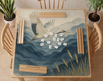 May include: A square mahjong mat featuring a printed illustration of a white crane flying over blue layered mountains and golden reeds. The mat includes four wooden tile racks placed along the edges, with several white mahjong tiles scattered across the center.