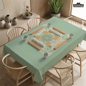 May include: A light green rectangular tablecloth with a floral design in the center, surrounded by wooden mahjong tiles and small white cups. The table is set for a game, with wooden chairs around it.