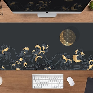 May include: A large, rectangular desk mat with a dark gray background and a gold wave design. The waves are stylized and reminiscent of Japanese art. A gold circle with a repeating pattern is also featured. The mat is shown on a wooden desk with a computer and accessories.