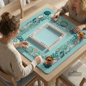 May include: A wooden square table with a light blue Mahjong mat decorated with seashells and coral. Two people are playing Mahjong, with tiles and drinks visible. The mat has the text "DESKNEKO" at the bottom.