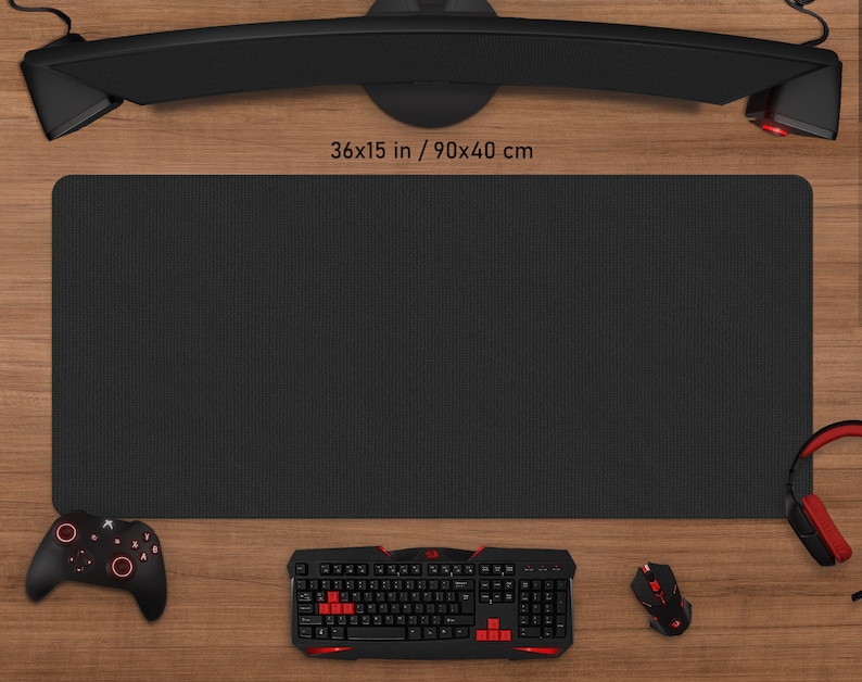 May include: A black rectangular gaming mouse pad, measuring 36 x 15 inches (90 x 40 cm), sits on a wooden surface. A black keyboard, mouse, controller, and headset with red accents are arranged around the pad. A curved monitor is above the pad.