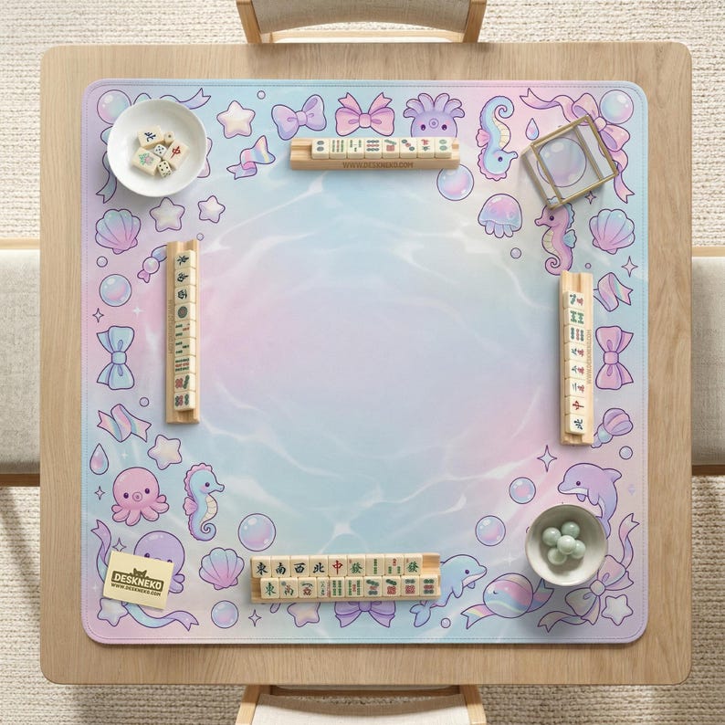 May include: A square mahjong game mat with a pastel ocean-themed design. The mat features illustrations of sea creatures, bows, and bubbles. Includes mahjong tiles, dice, and a small bowl with green balls. The text "DESKNEKO" is visible.