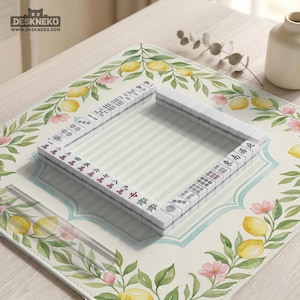 May include: A white Mahjong set arranged on a floral-patterned mat with lemons and pink flowers. The mat has a light blue and white striped center. The tiles have Chinese characters and symbols. The brand name "DESKNEKO" is visible in the top left corner.