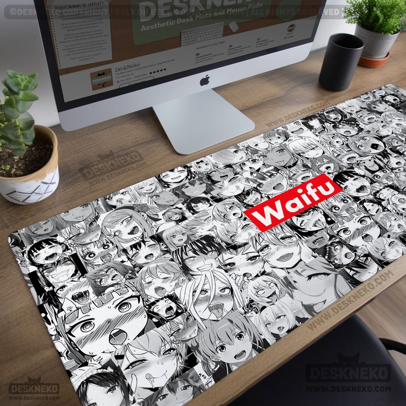 May include: A long rectangular desk mat featuring a black and white anime-style illustration of multiple faces. A red rectangle with the word "Waifu" in white is centered on the mat. The mat is on a wooden desk.