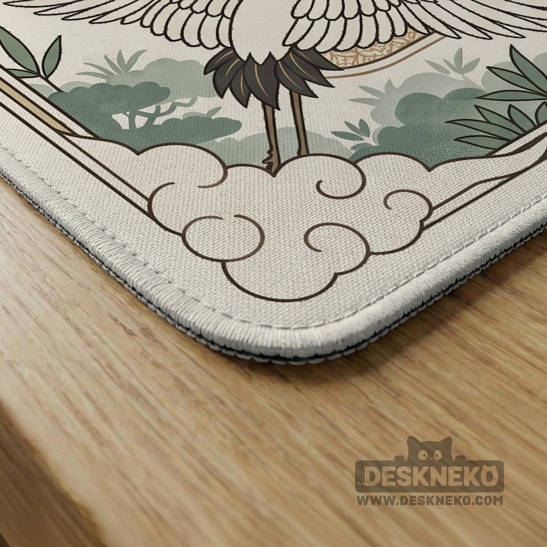 May include: A rectangular desk mat featuring a Japanese crane design. The mat has a cream-colored background with a detailed illustration of a crane, clouds, and foliage in shades of green and brown. The mat has a stitched edge.