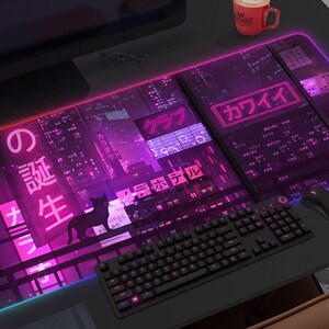 Op de afbeelding: Een groot, rechthoekig gaming-muismat met een neon paars en roze stadsgezicht ontwerp. De mat heeft Japanse tekst en een zwart kat silhouet. Een zwart toetsenbord en muis liggen op de mat.