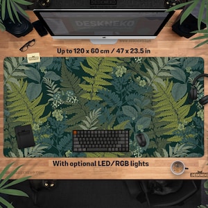 Pu&ograve; includere: Un grande tappetino da scrivania rettangolare con un design botanico con felci e altro fogliame in tonalit&agrave; di verde e blu. Il tappetino misura fino a 120 x 60 cm e include il testo "With optional LED/RGB lights".