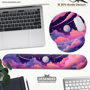 Pu&ograve; includere: Un'impostazione del computer con un laptop, un mouse e un poggiapolsi e un tappetino per mouse abbinati. Gli accessori presentano un design vibrante di un cielo notturno con pianeti, nuvole e stelle. L'indirizzo del sito web "WWW.DESKNEKO.COM" &egrave; visibile.